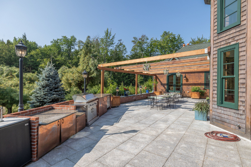 Beautiful view of a patio of a luxurious mansion surrounded by evergreen trees on a sunny day